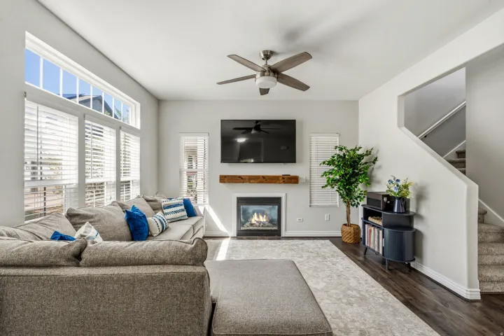 Living area with large windows, a ceiling fan, a fireplace with a wood mantle, and dark wood-finish flooring