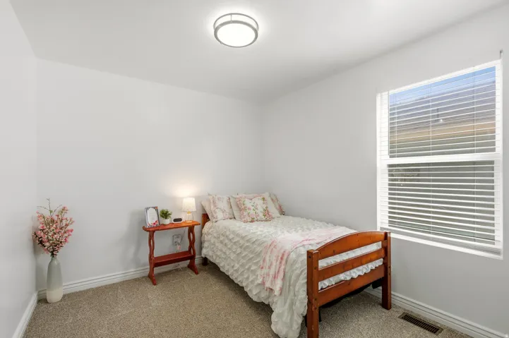 Bright secondary bedroom featuring hardwood-finish flooring, horizontal blinds on large window with natural light, wood-frame bed frame, and neutral wall finishes