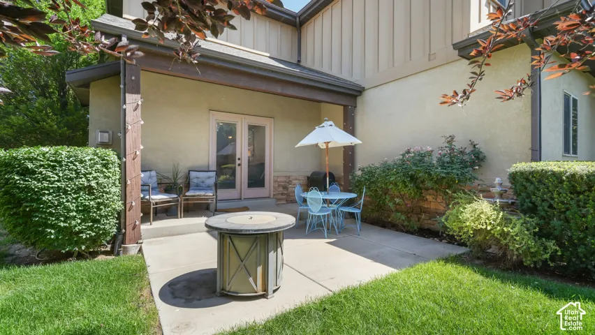 Private patio featuring a covered area, concrete flooring, exterior doors, and surrounding greenery