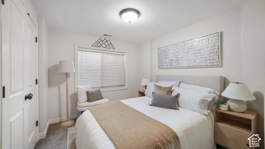 Bedroom featuring a window with horizontal blinds, overhead flush mount lighting, and light-toned carpet flooring