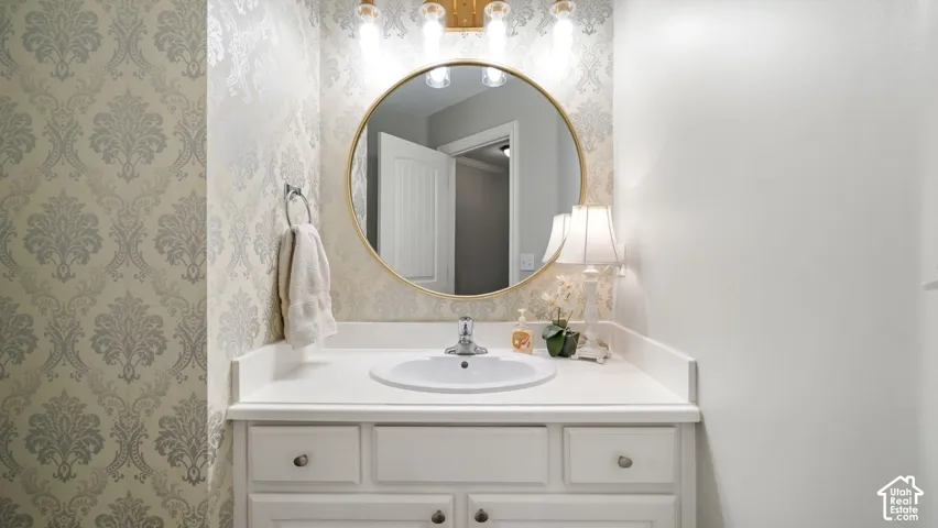 Vanity with an integrated sink and white countertop, framed by patterned wallpaper and a gold-toned mirror