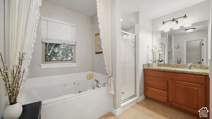 Master Bathroom featuring a jetted soaking tub, separate glass-enclosed shower, wood-finish vanity with an integrated sink, and a light-colored countertop