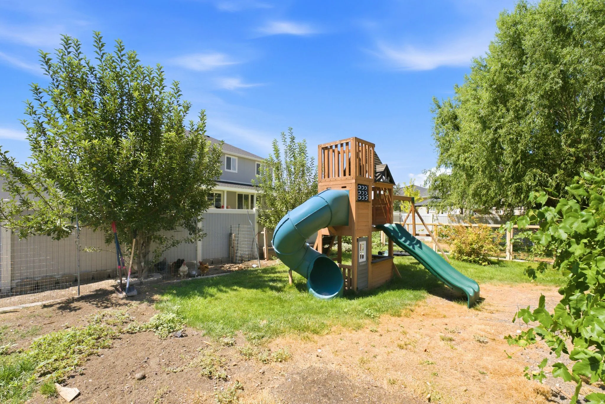 Expansive backyard area featuring a wooden play structure with a tube slide and open slide