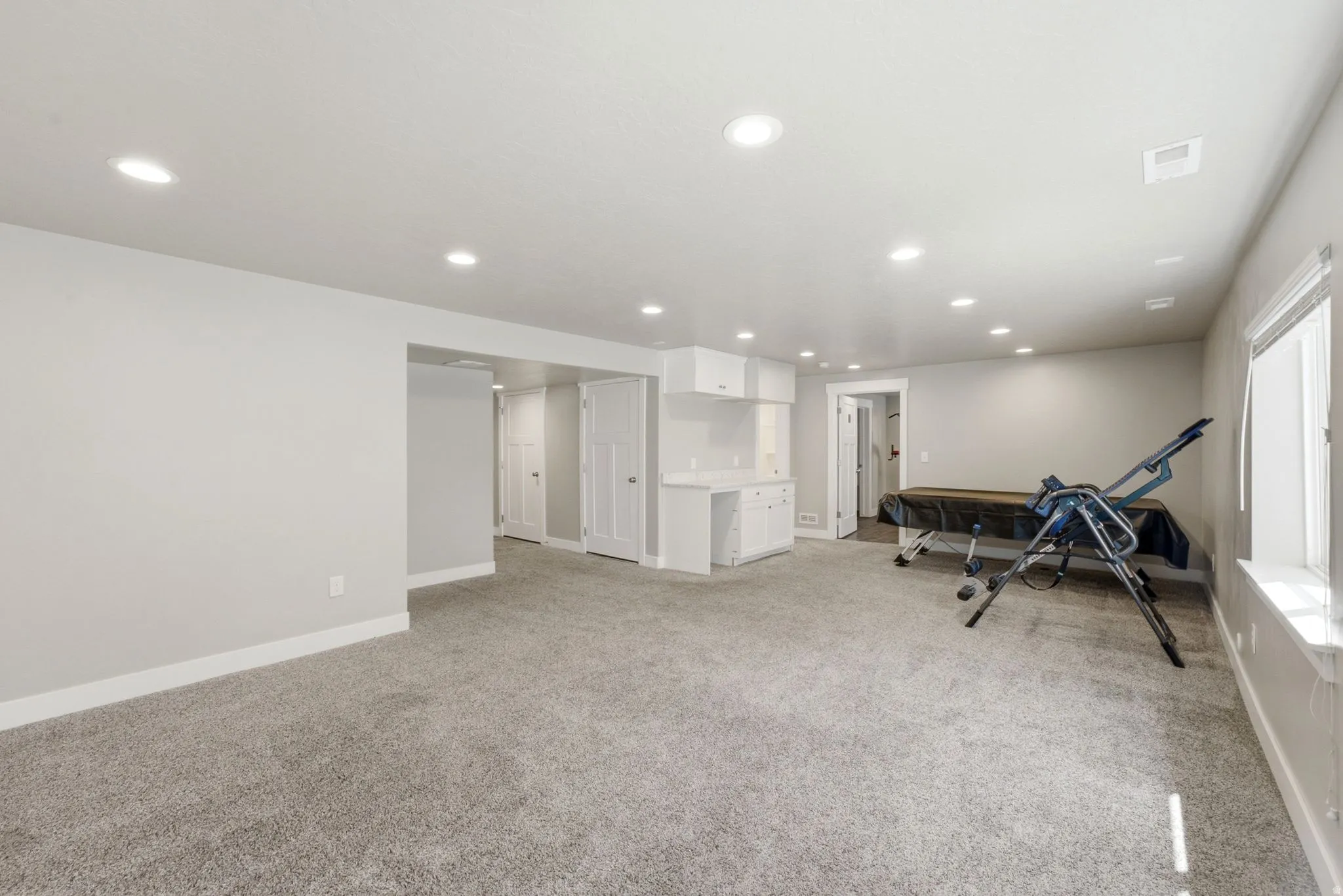 Spacious carpeted room featuring recessed lighting, a built-in wet bar with white cabinetry, a window with natural light, and ample white trim throughout
