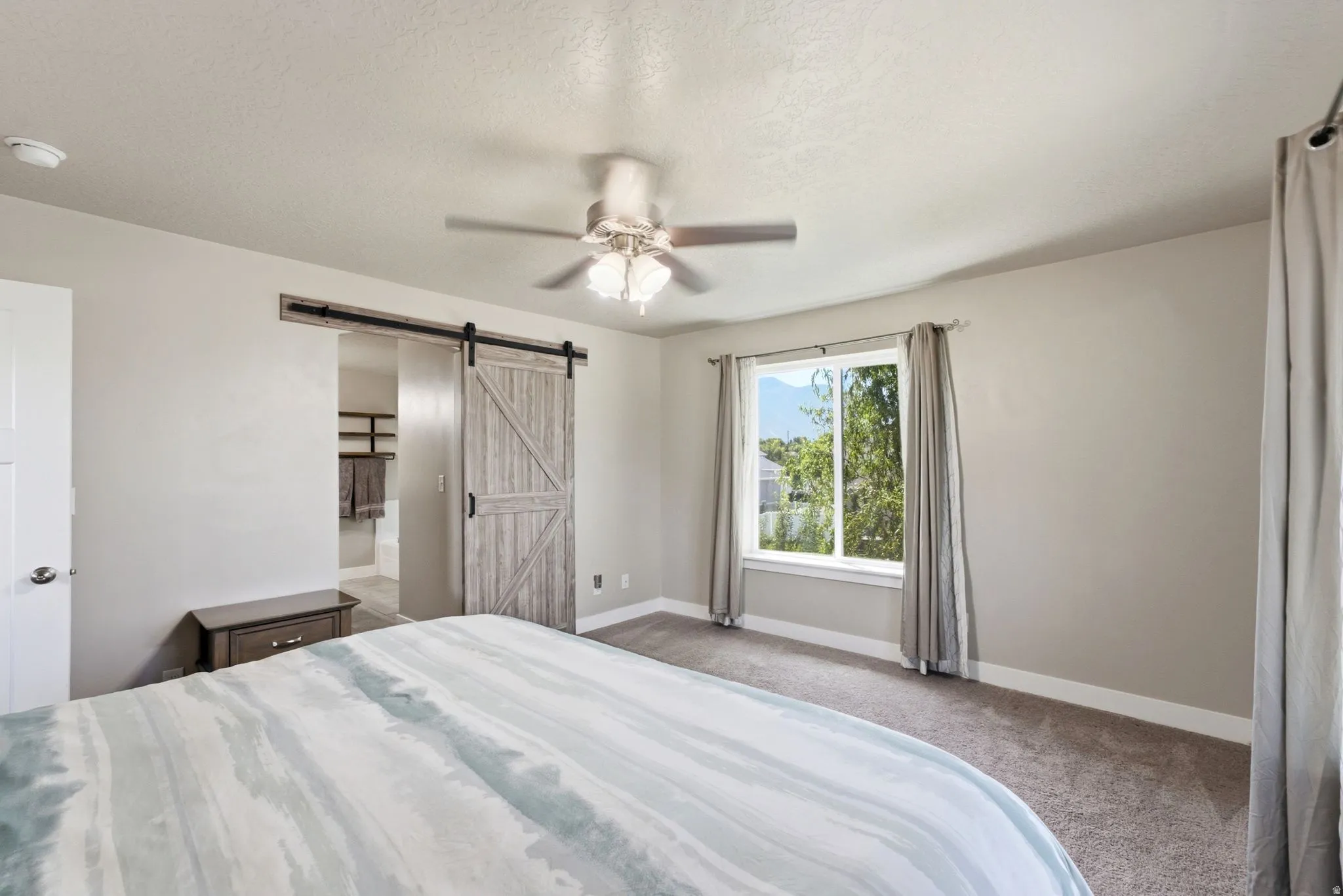 Room featuring a window with exterior tree scenery, a ceiling fan with integrated lighting, and a wood-finish barn door