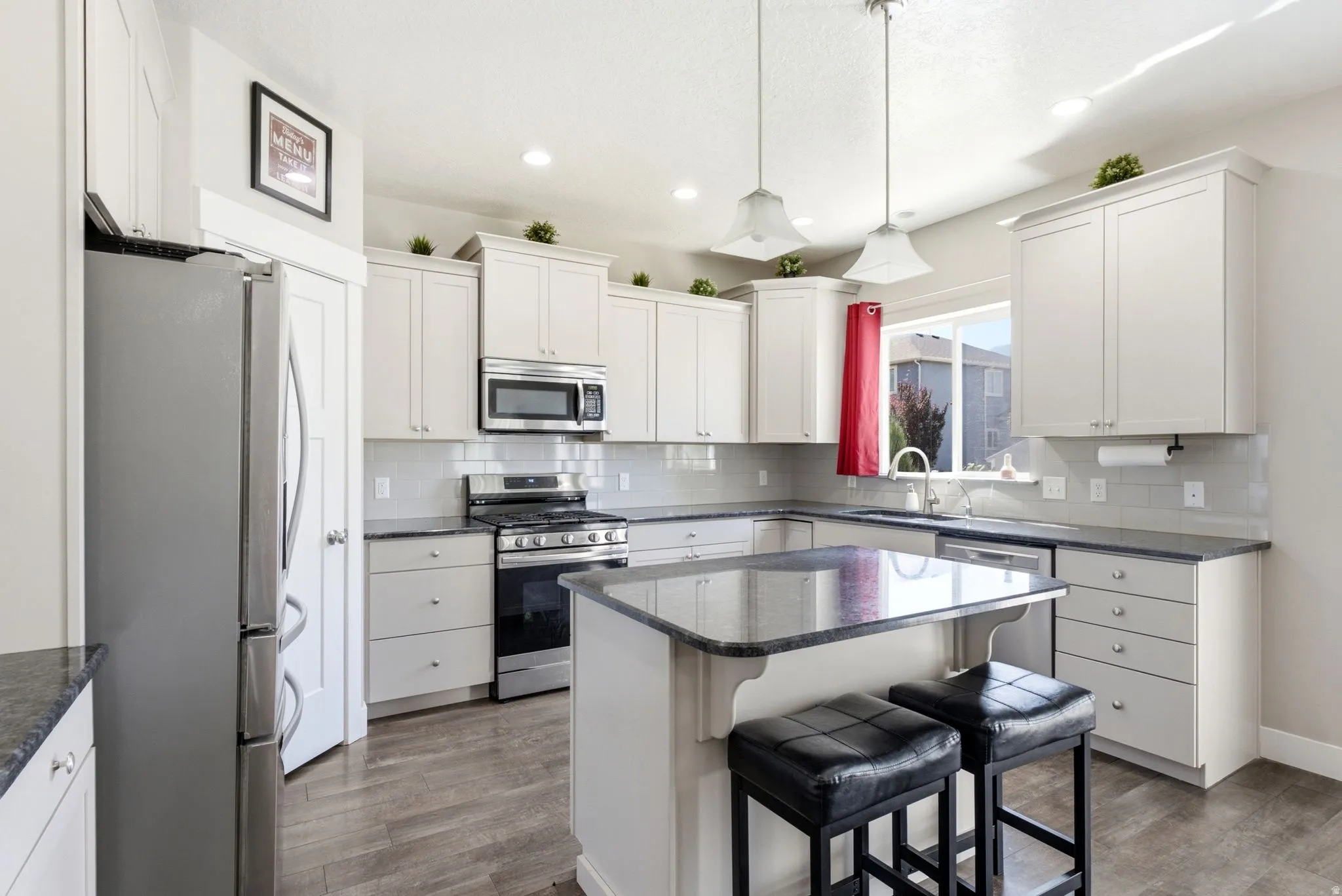Kitchen featuring a central island with countertop seating, light-toned cabinetry, stainless steel appliances, and wood-finish flooring