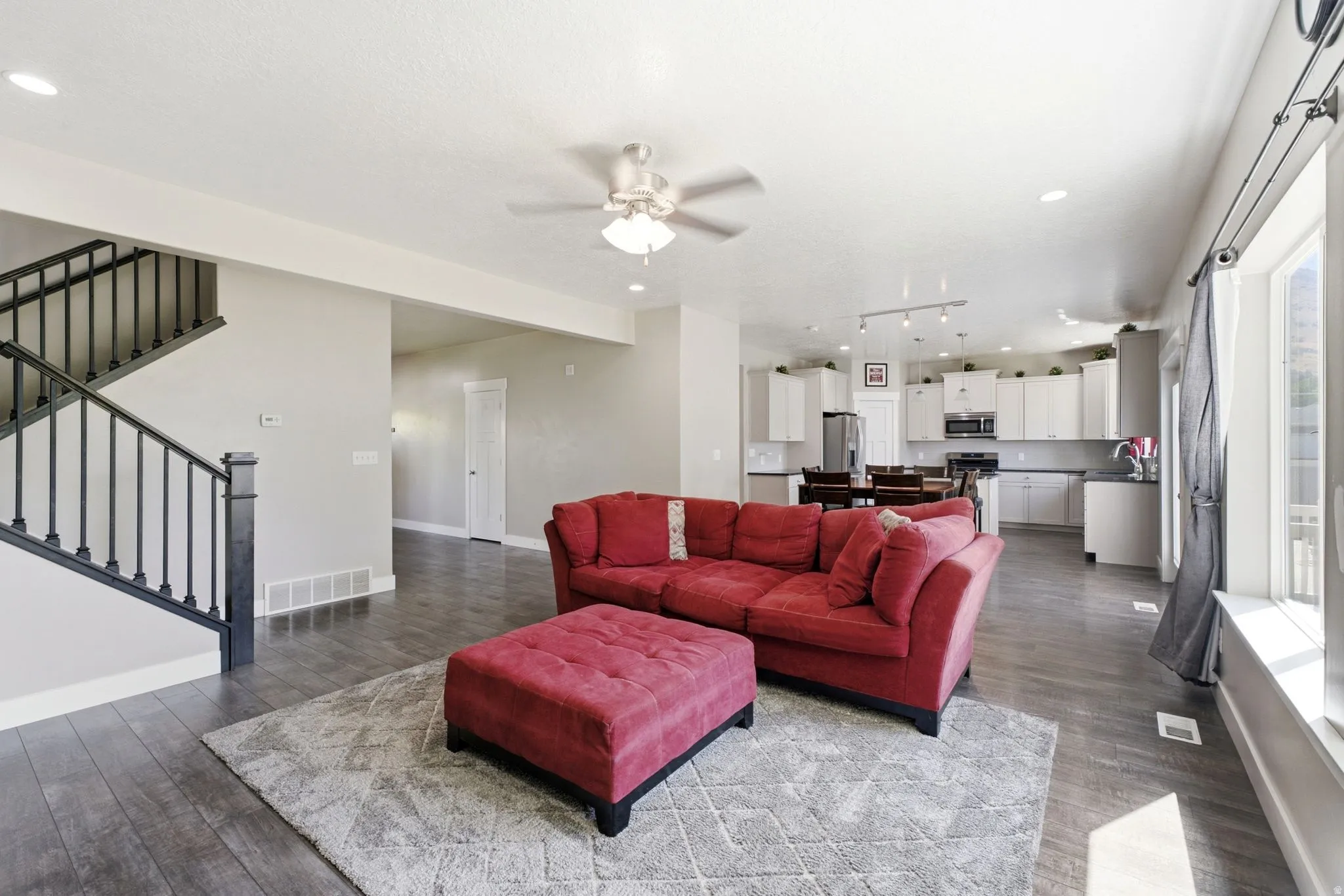 Open-concept main level featuring wood-finish flooring, a contemporary staircase with dark balusters, recessed lighting, and a ceiling fan