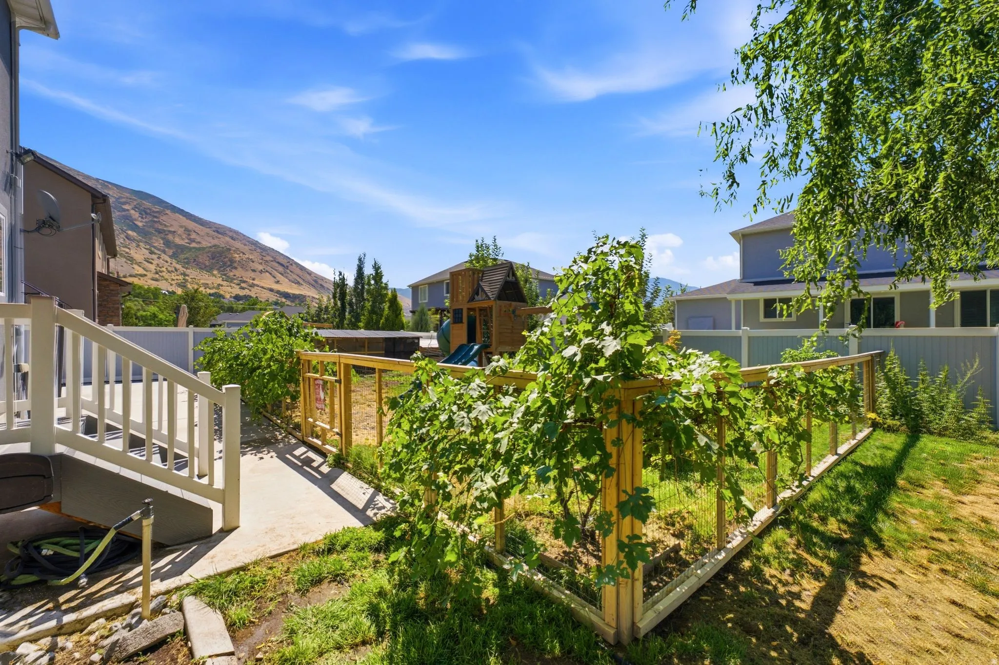 Expansive backyard featuring a concrete patio, white railing, natural grass, and a wood-framed garden area