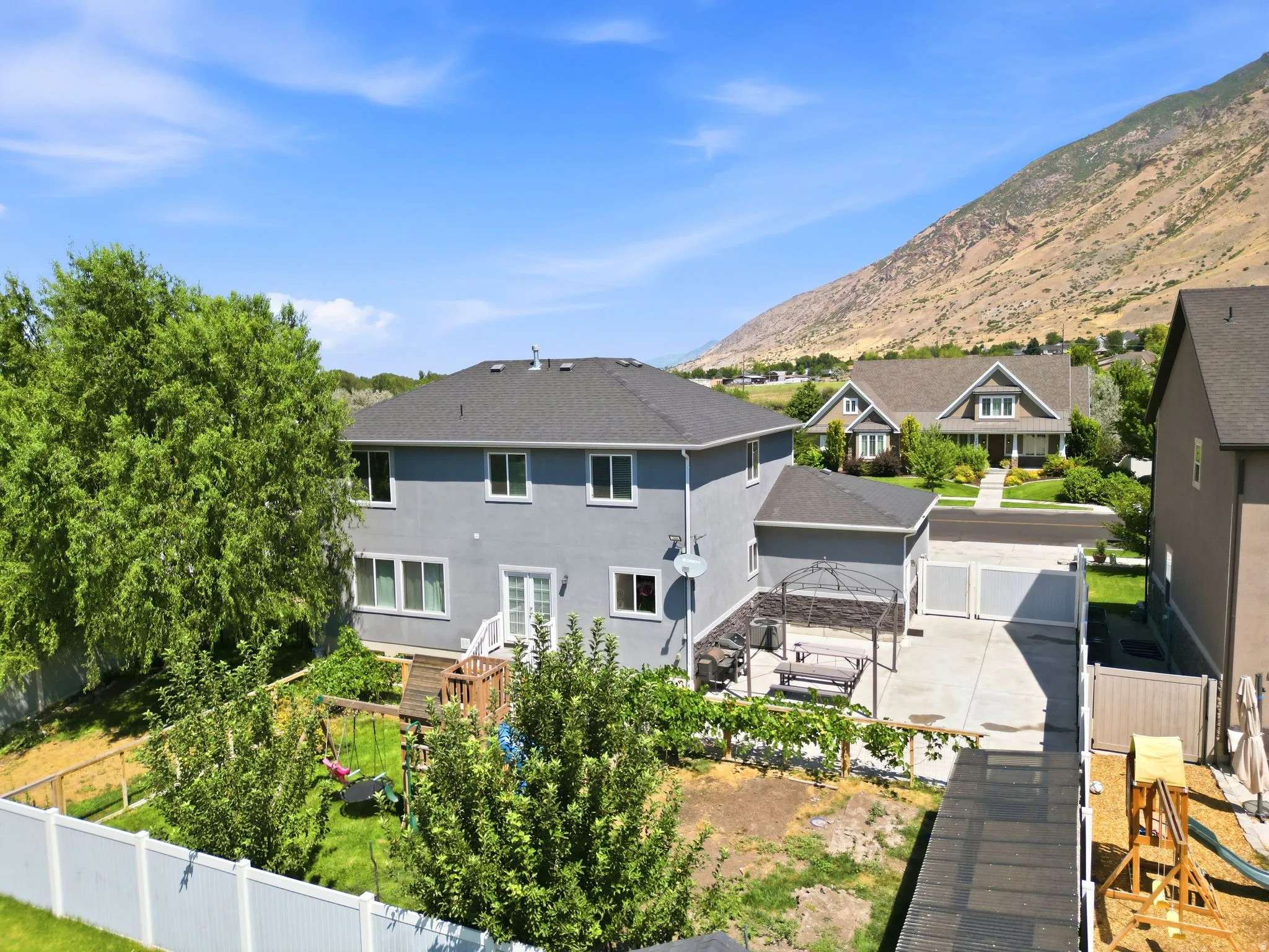 Spacious rear exterior featuring a concrete patio, white privacy fencing, a multi-level deck with white railings, and mature landscaping