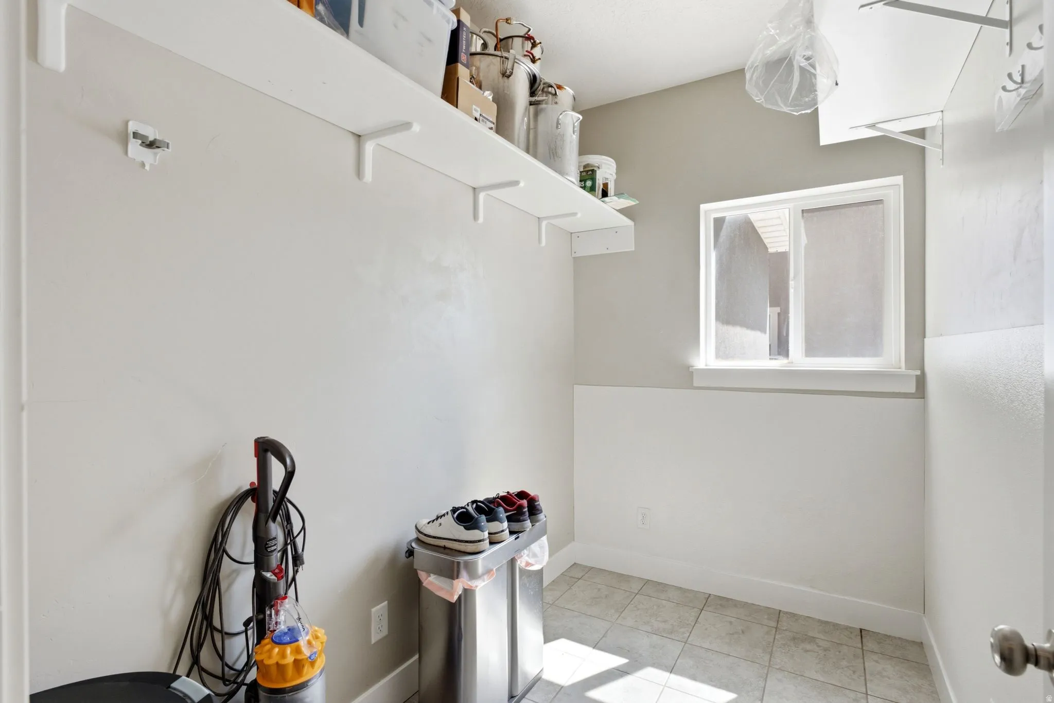 Utility space featuring light-toned walls, a white window frame, and tiled flooring