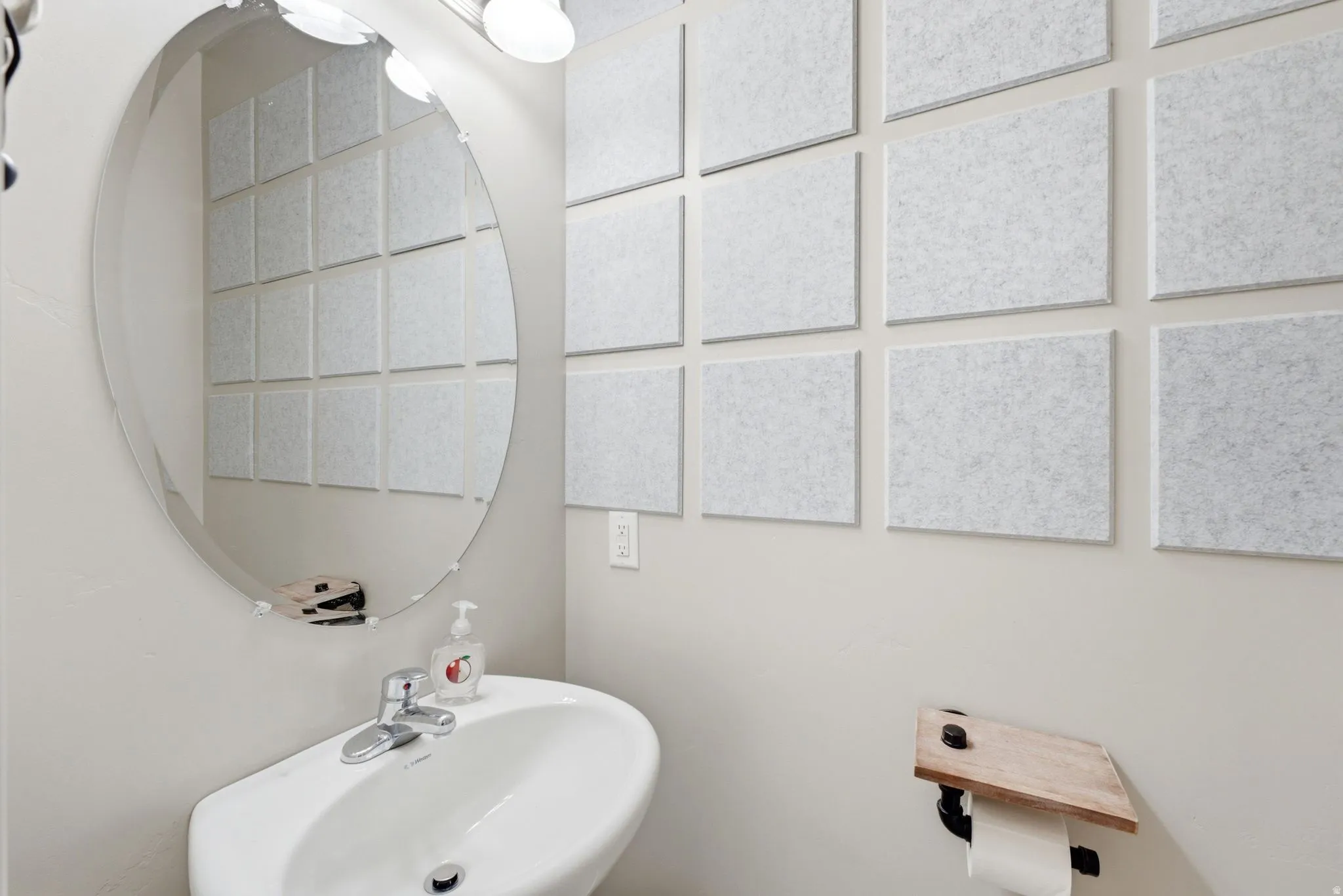 Oval frameless mirror over a white wall-mounted pedestal sink with a chrome faucet