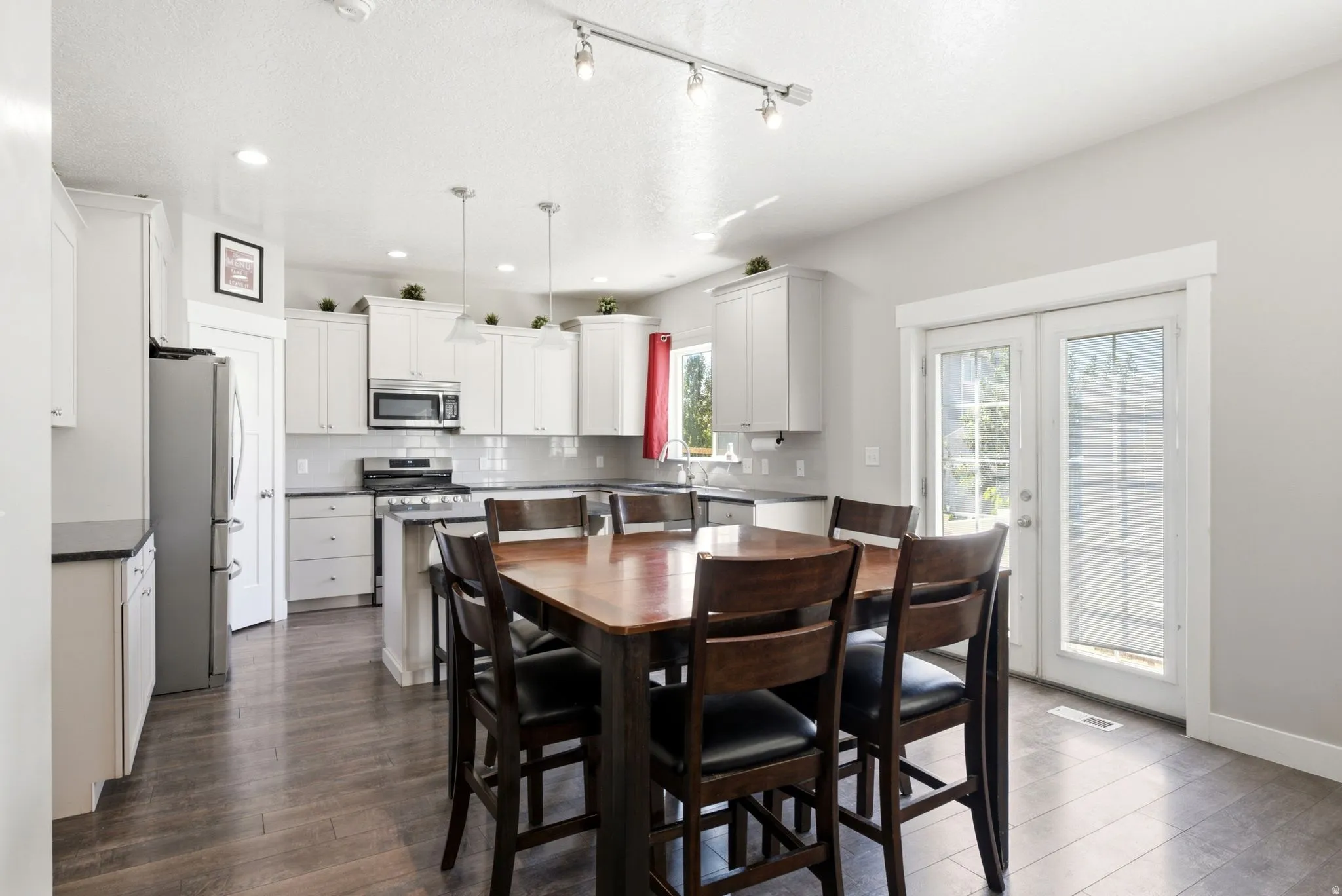 Open-concept kitchen and dining area featuring wood-finish flooring, white cabinetry, dark countertops, and stainless steel appliances