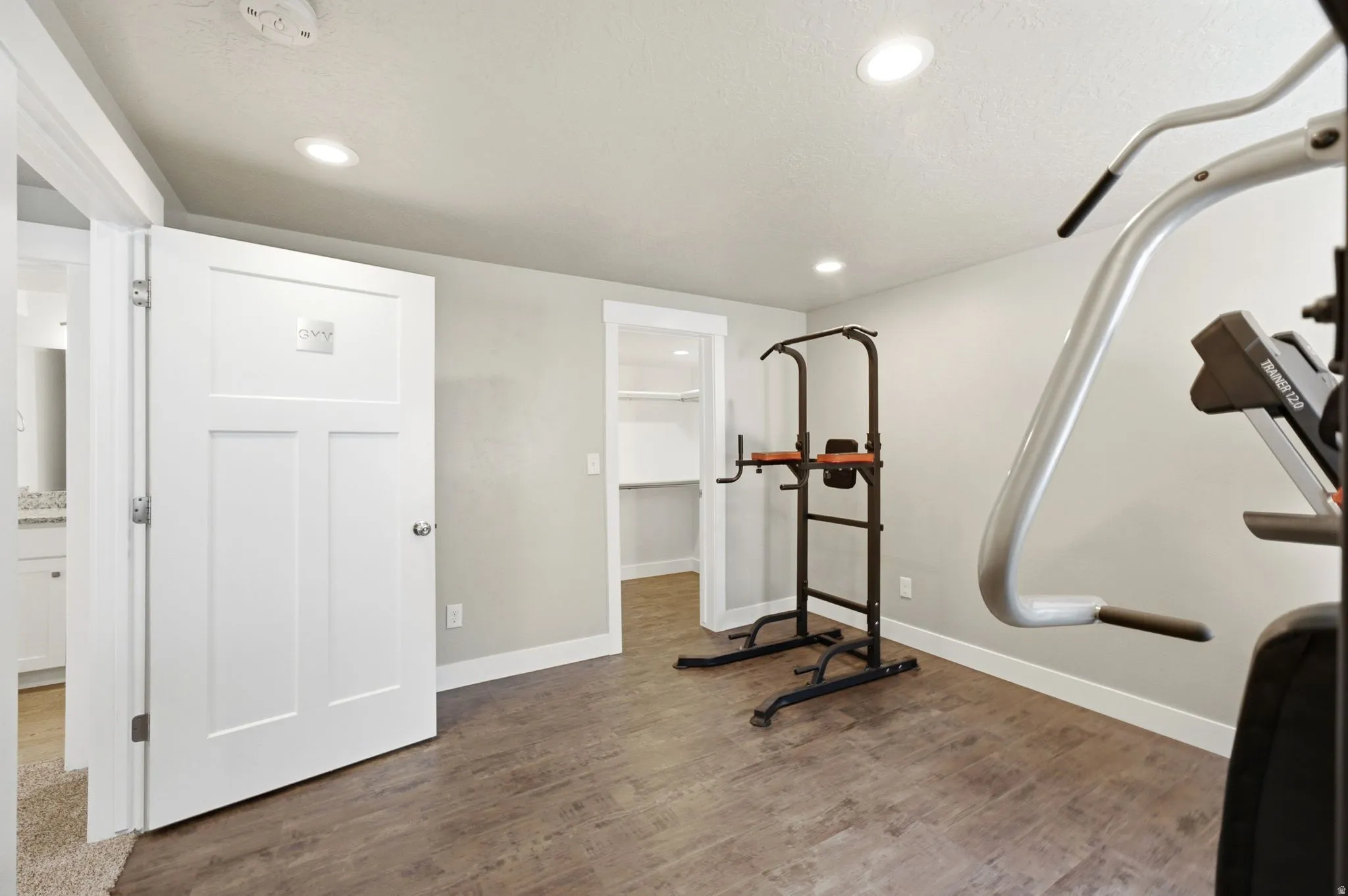 Spacious room with recessed lighting, wood-finish flooring, light gray walls, and white baseboards