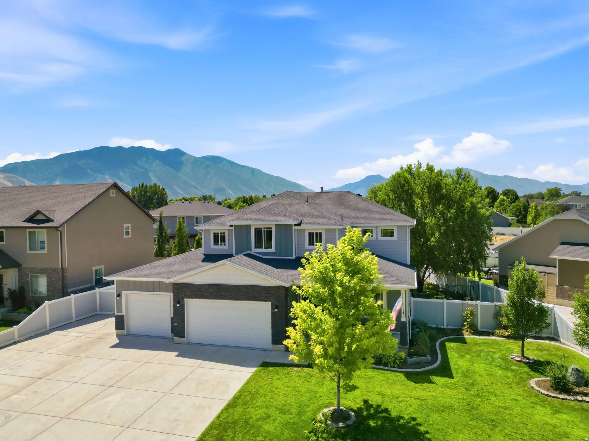 Two-story residence featuring light blue siding with dark stone accents, a dark shingle roof, and a three-car garage