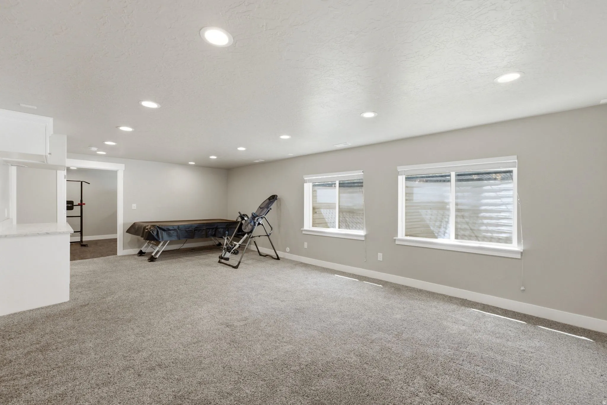 Spacious room featuring neutral carpeting, recessed lighting, and two windows with white blinds