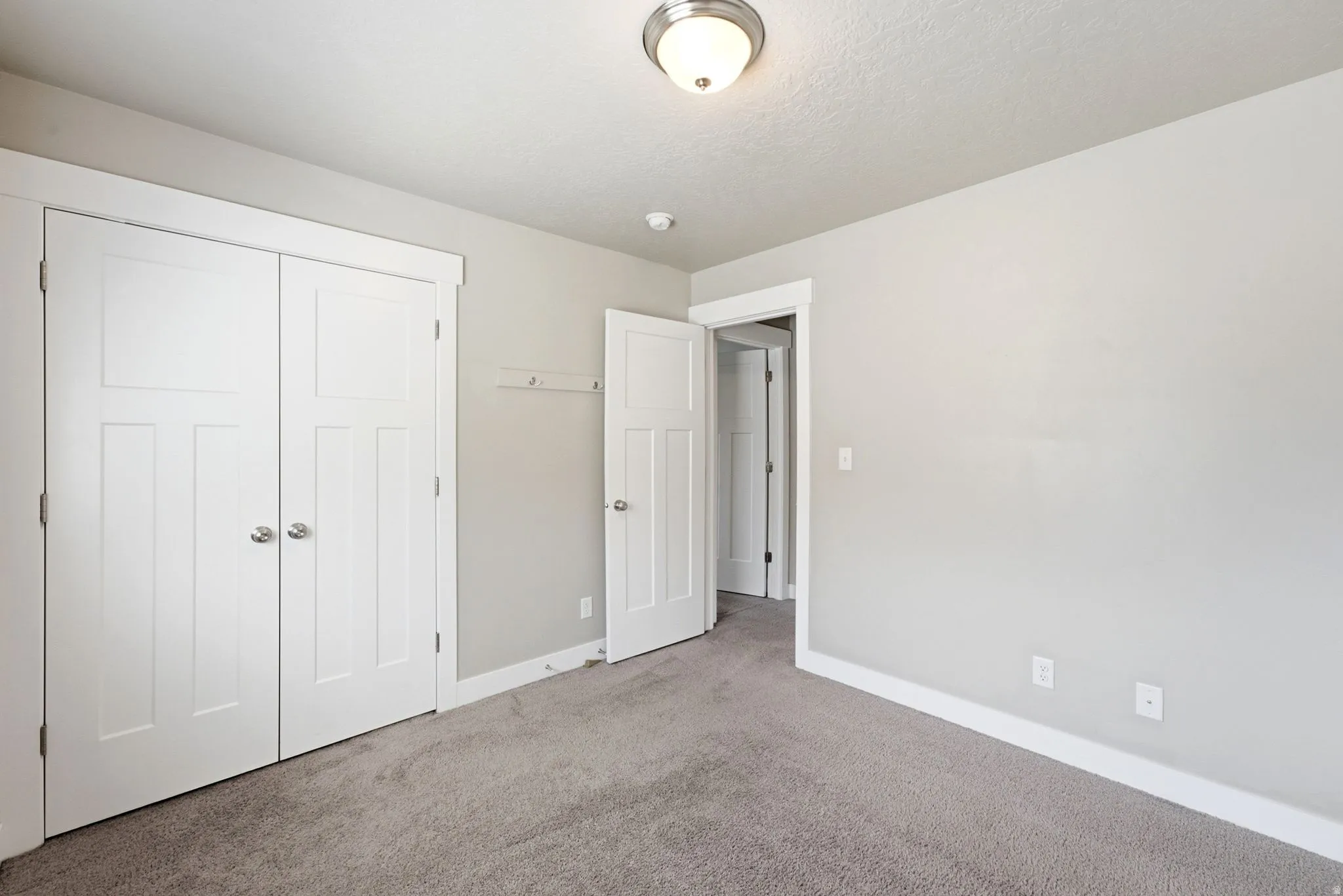 Carpeted interior room with light grey walls, white baseboards, and a semi-flush ceiling light fixture