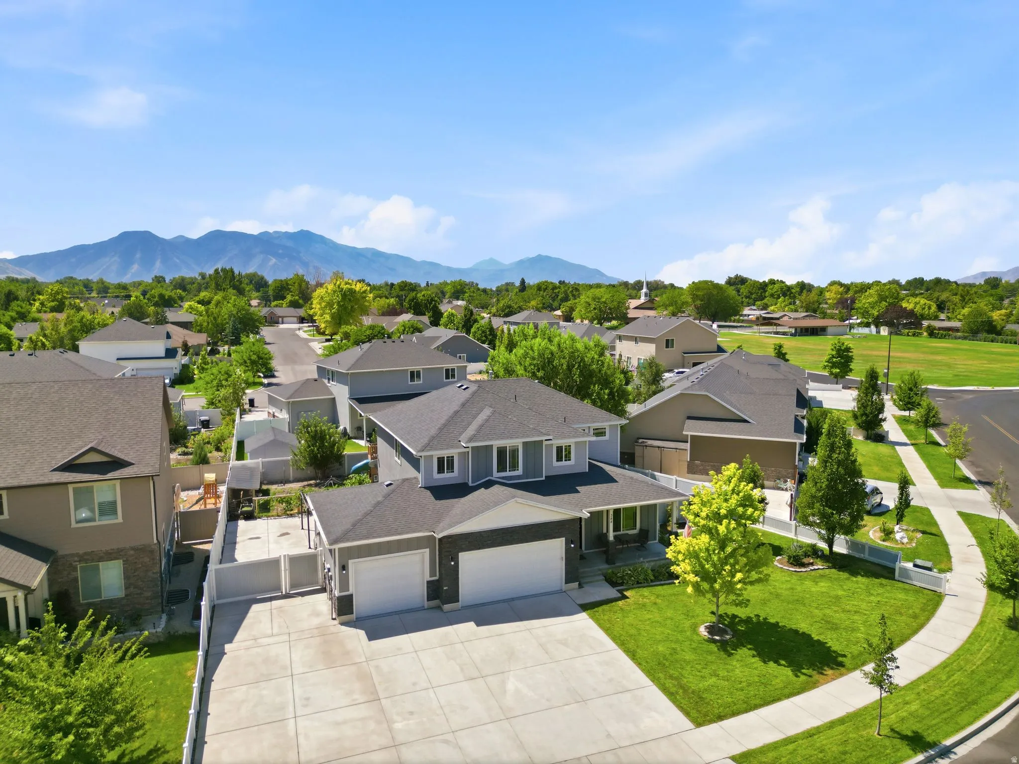 Contemporary residence featuring a two-car garage, mature landscaping, and a mountain backdrop