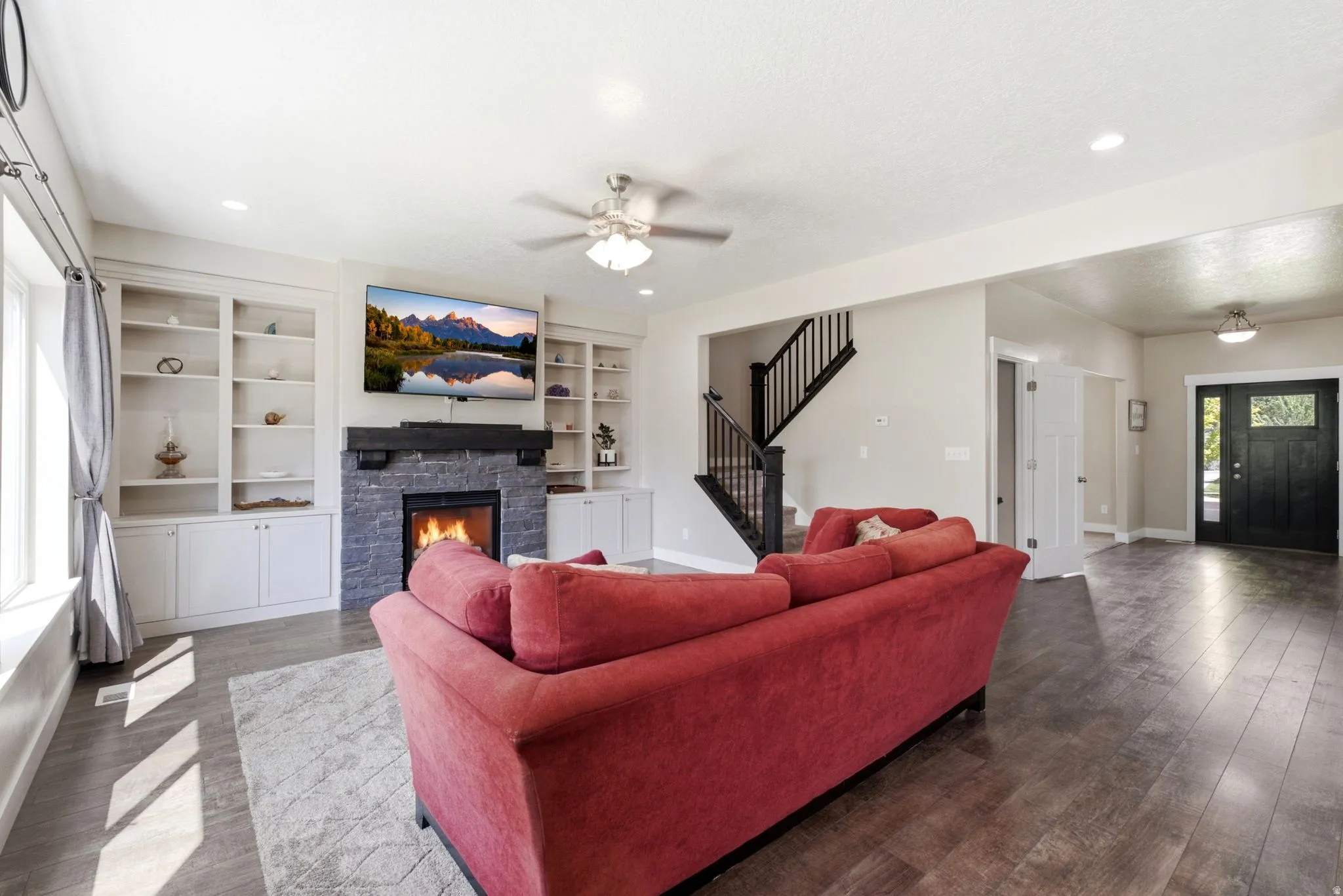 Spacious living area featuring a stone-clad fireplace with a dark wood mantel, built-in shelving, and wood-finish flooring