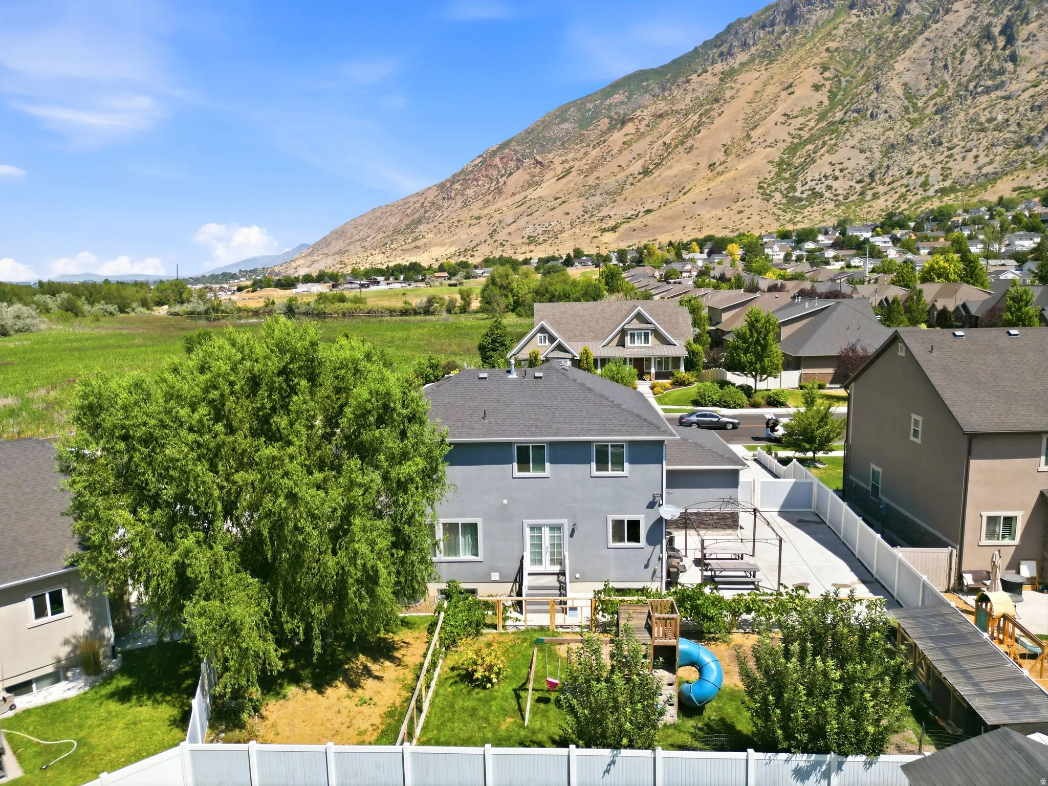 Rear exterior featuring a patio with a pergola, fenced backyard with mature landscaping, and a vibrant green lawn