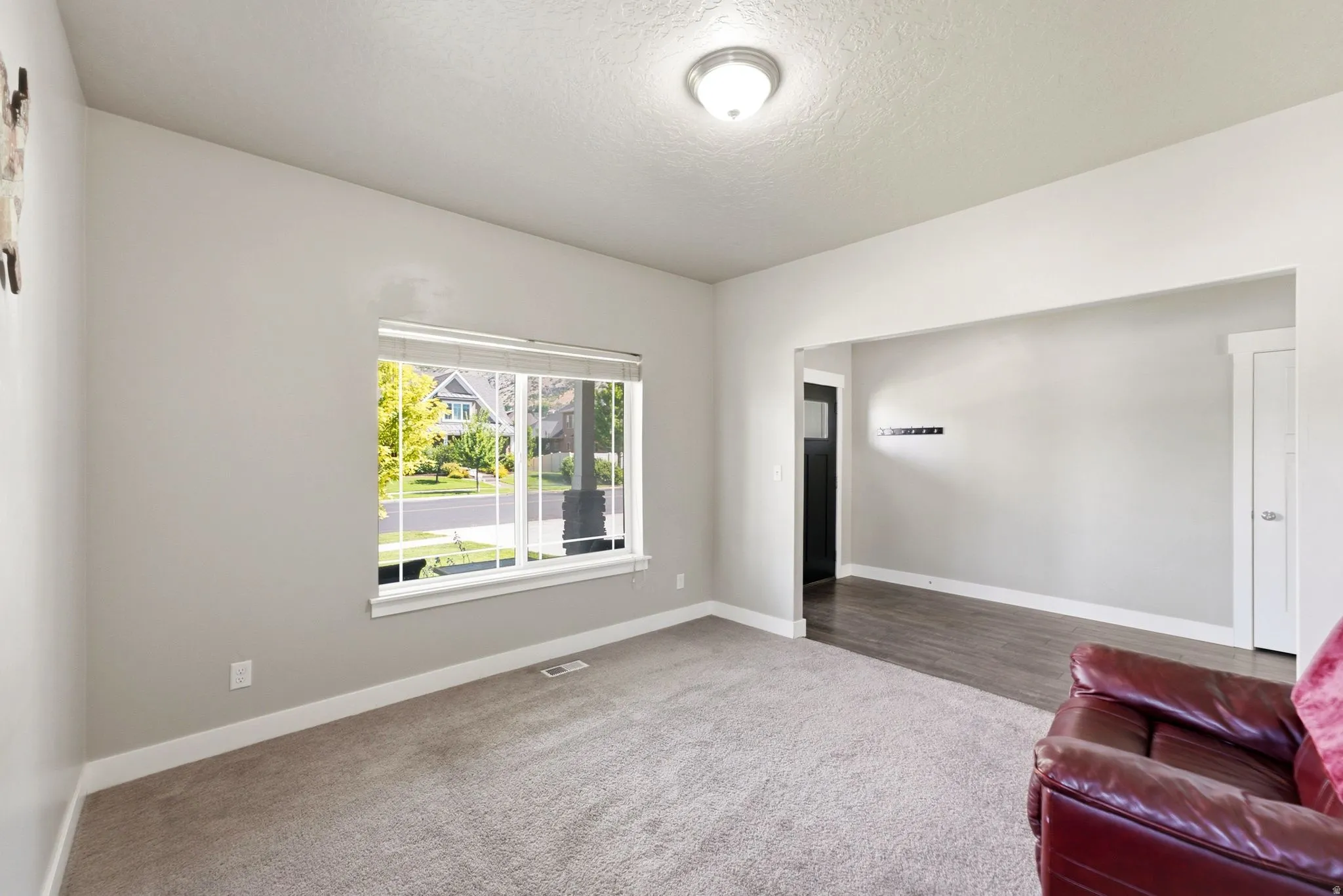Carpeted living space featuring a large window, light gray wall paint, white baseboards, and a semi-flush ceiling light fixture