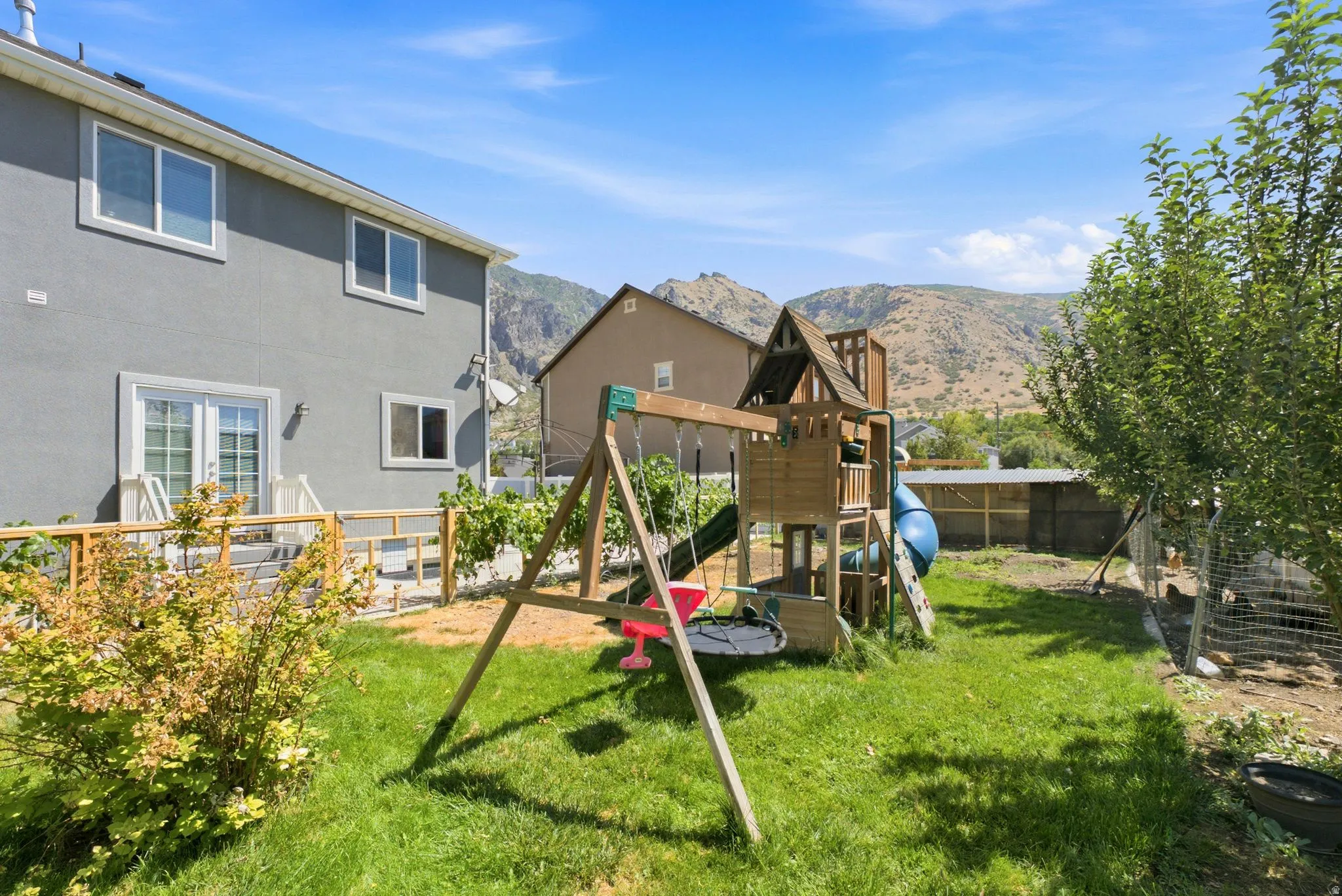 Backyard featuring a green lawn, established trees, and a raised wooden deck with white railing