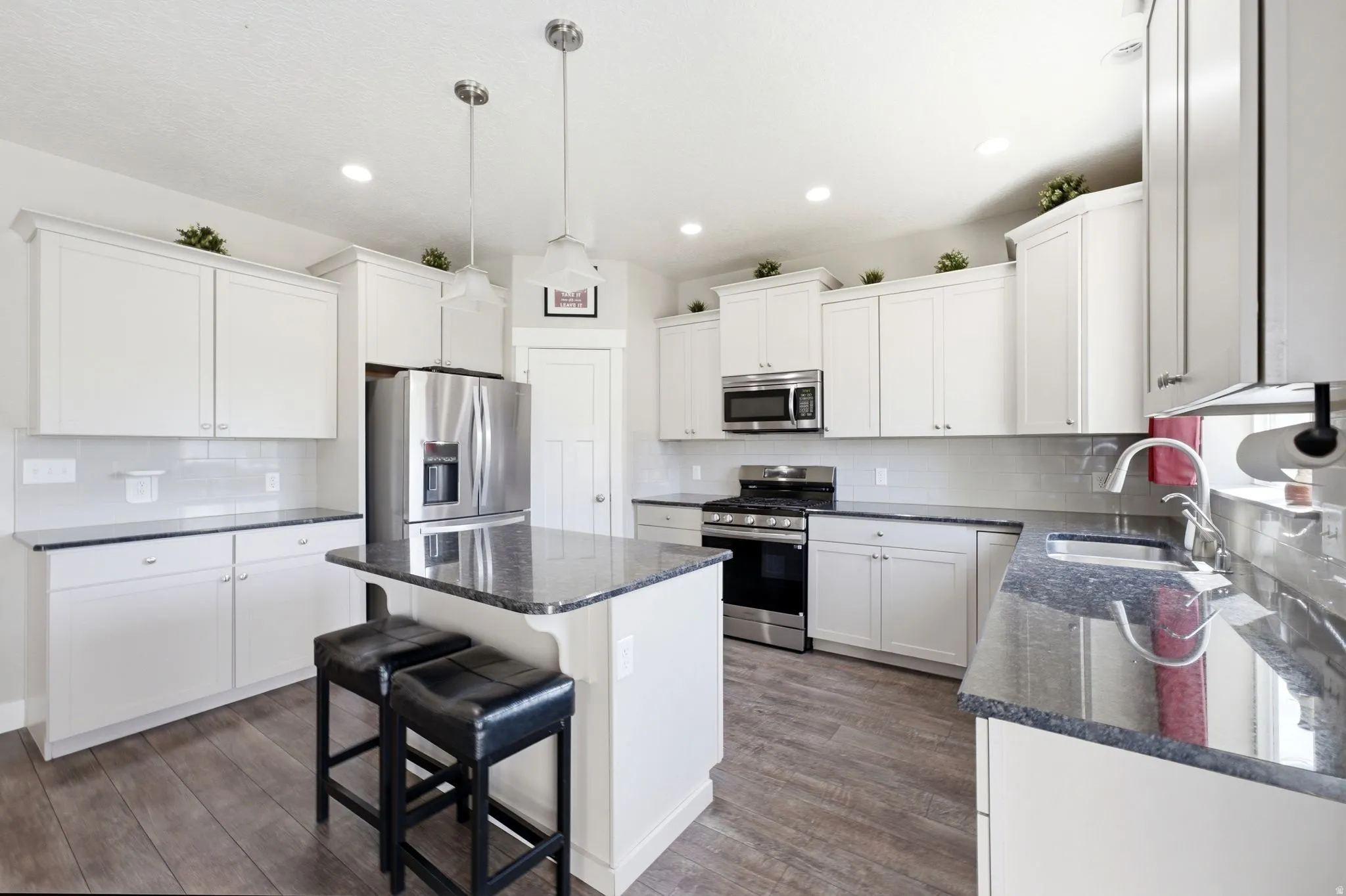 Kitchen featuring white cabinetry, dark stone countertops, stainless steel appliances, wood-finish flooring, and recessed lighting