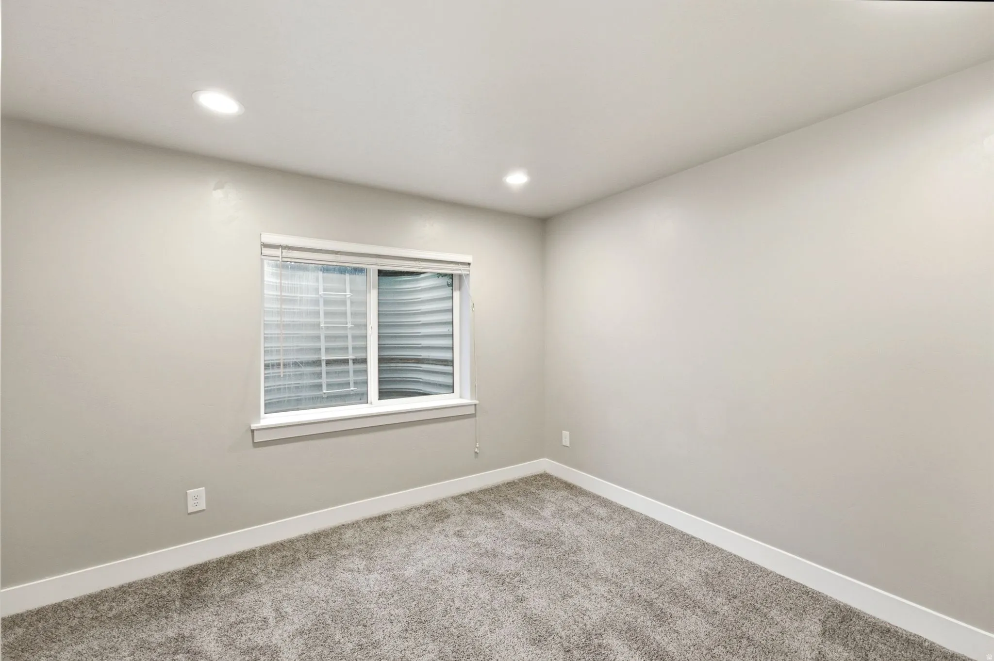 Carpeted room featuring a white-framed window, recessed lighting, neutral wall paint, and white baseboards