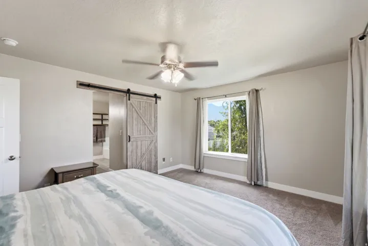 Room featuring a window with exterior tree scenery, a ceiling fan with integrated lighting, and a wood-finish barn door