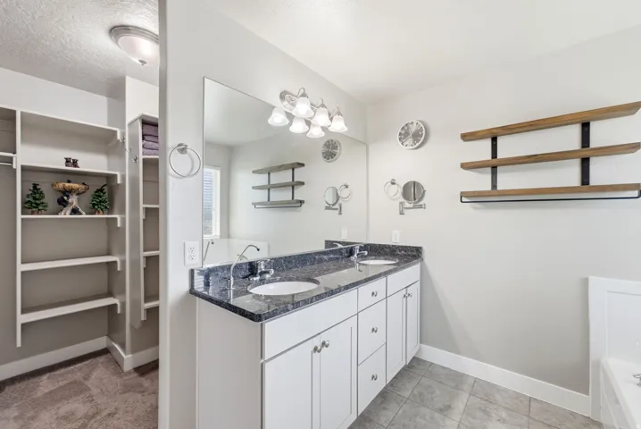 Dual vanity with white cabinetry and dark speckled countertops, undermount sinks, and a large wall mirror