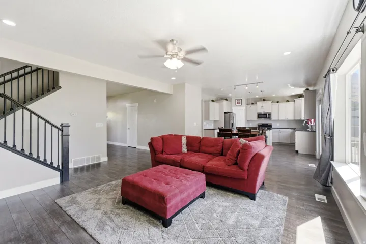 Open-concept main level featuring wood-finish flooring, a contemporary staircase with dark balusters, recessed lighting, and a ceiling fan