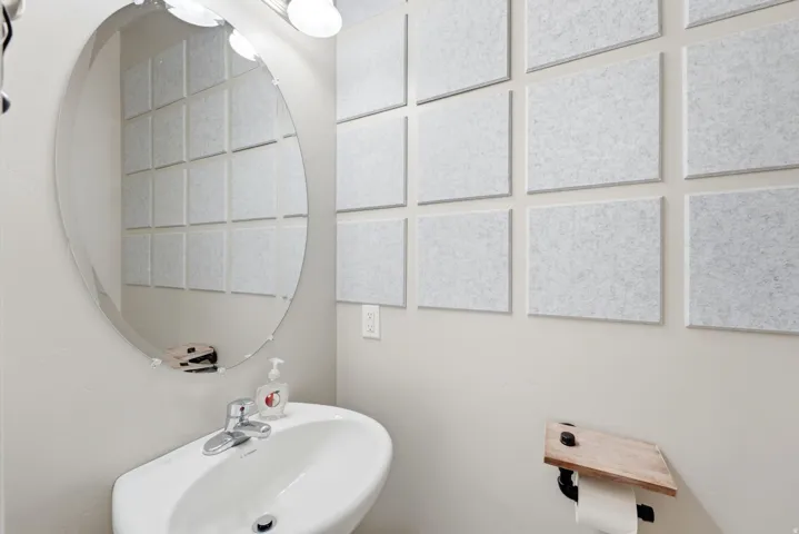 Oval frameless mirror over a white wall-mounted pedestal sink with a chrome faucet