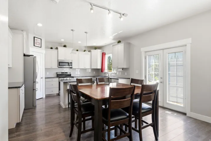Open-concept kitchen and dining area featuring wood-finish flooring, white cabinetry, dark countertops, and stainless steel appliances