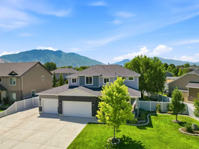 Two-story residence featuring light blue siding with dark stone accents, a dark shingle roof, and a three-car garage