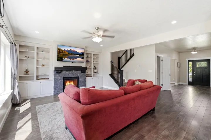 Spacious living area featuring a stone-clad fireplace with a dark wood mantel, built-in shelving, and wood-finish flooring