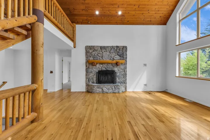 Spacious room featuring a stone fireplace with a substantial wood mantel, warm wood-finish flooring, and a vaulted wood-paneled ceiling