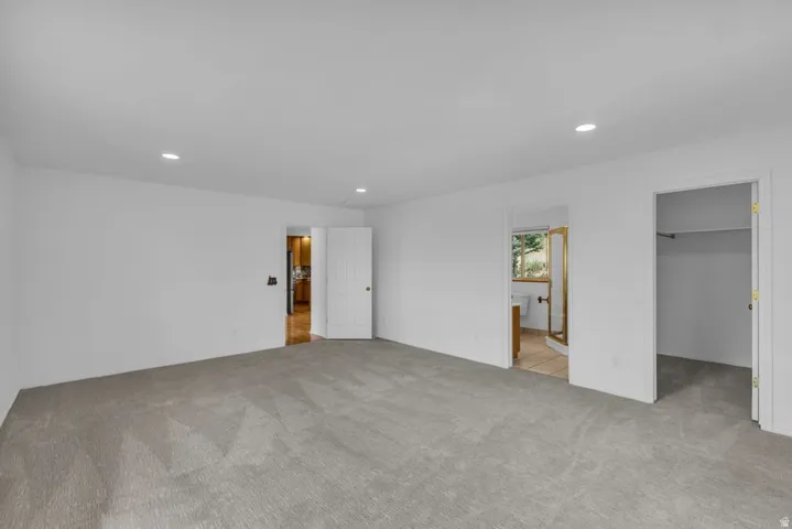 Spacious room with light gray carpeting, recessed lighting, white walls, and a white paneled door