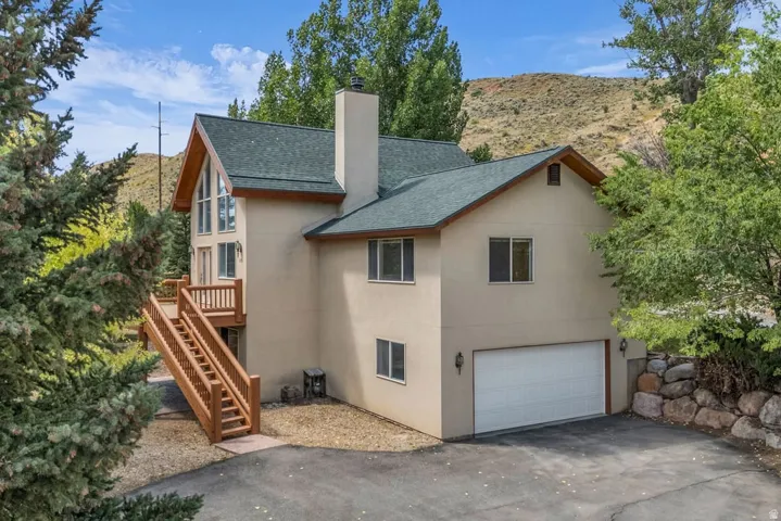 Stucco exterior residence featuring an attached garage, pitched roof, and a prominent chimney