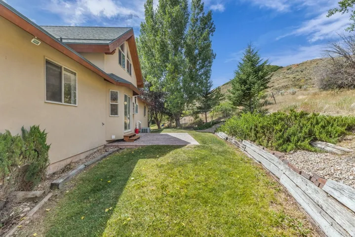 Expansive backyard featuring a stone paver patio, a terraced landscape with timber retaining walls, and a combination of manicured lawn and natural shrubbery