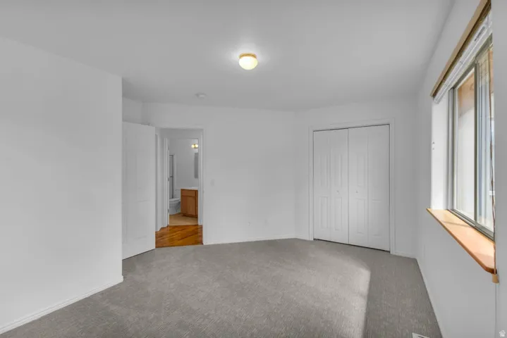 Spacious room featuring neutral carpeting, a large window with a wood sill, and a bi-fold closet