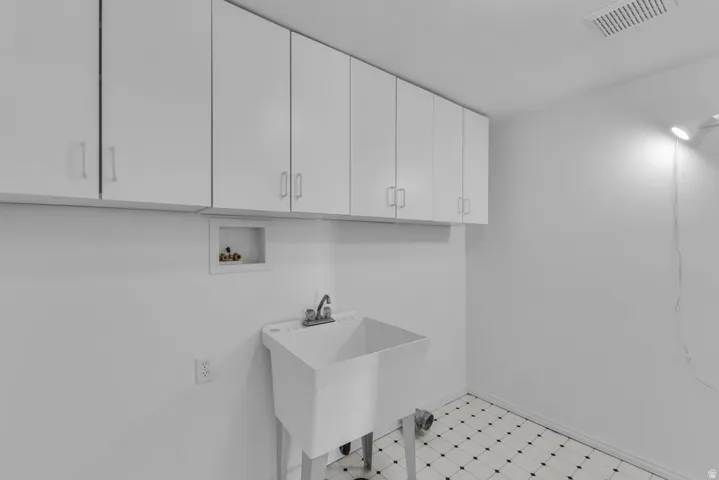 Utility room featuring extensive white cabinetry, a large utility sink, classic patterned floor tiles, and a ceiling-mounted ventilation grate