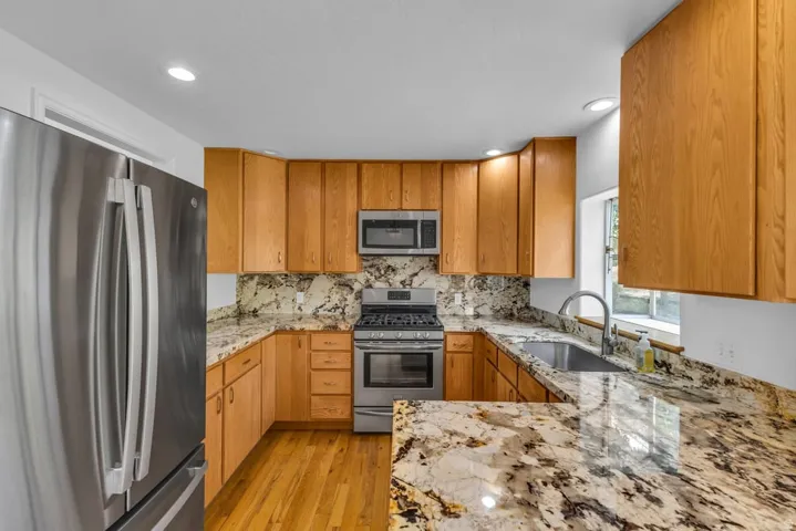 Kitchen featuring stainless steel appliances, wood-finish cabinetry, stone countertops, and a full-height stone backsplash