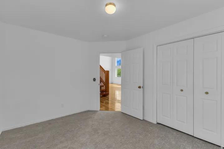 Carpeted room featuring white walls, a flush-mount ceiling light, and bi-fold closet doors with brass hardware