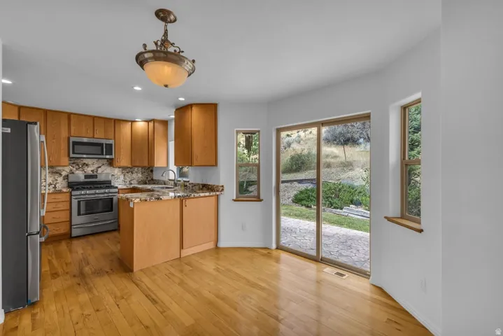 Kitchen featuring light wood cabinetry, stainless steel appliances, and a granite-style countertop with a matching backsplash