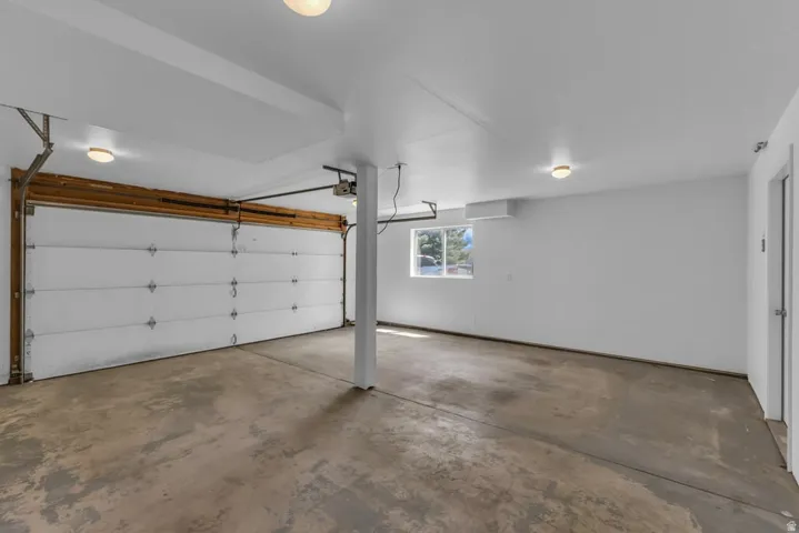 Spacious garage featuring a concrete floor, overhead lighting, a white sectional garage door, a window, and a wall-mounted unit