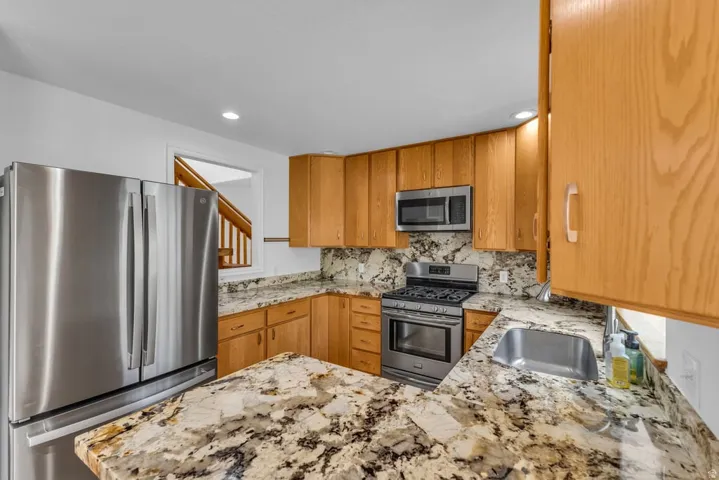Kitchen featuring wood cabinetry, stainless steel appliances, speckled stone countertops, and a stainless steel sink