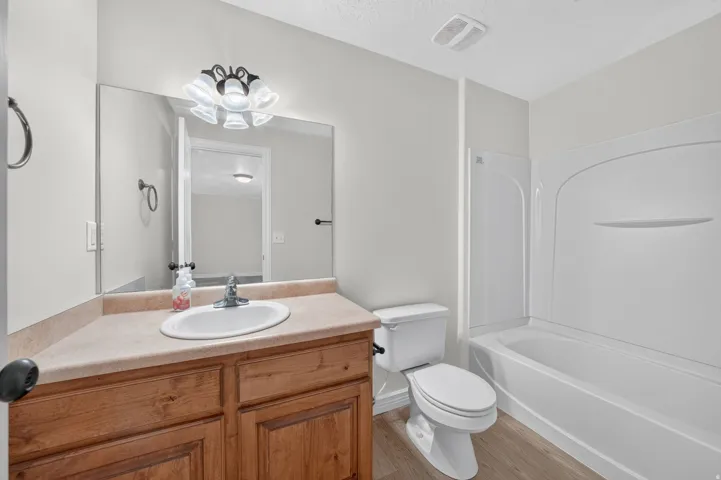 Bathroom featuring a white tub and shower surround, wood-finish vanity with an integrated sink, and a large wall-mounted mirror