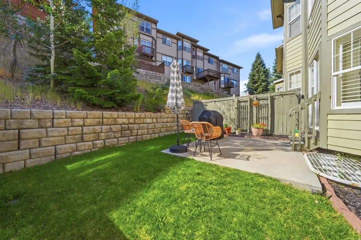 Private outdoor patio featuring a concrete surface, manicured lawn, and a stone retaining wall