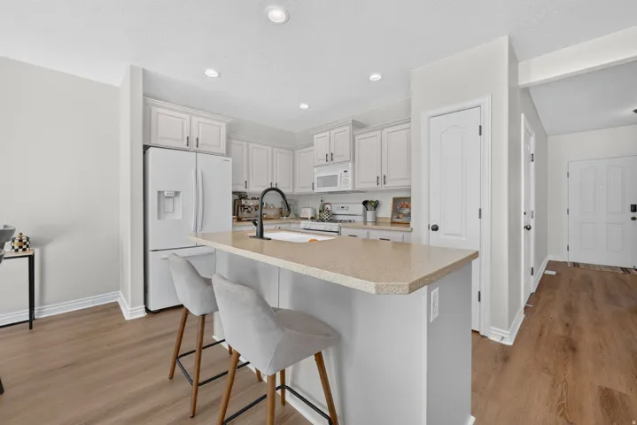 Kitchen featuring white cabinetry, a central island with countertop seating, a black gooseneck faucet, light-toned flooring, and recessed ceiling lighting
