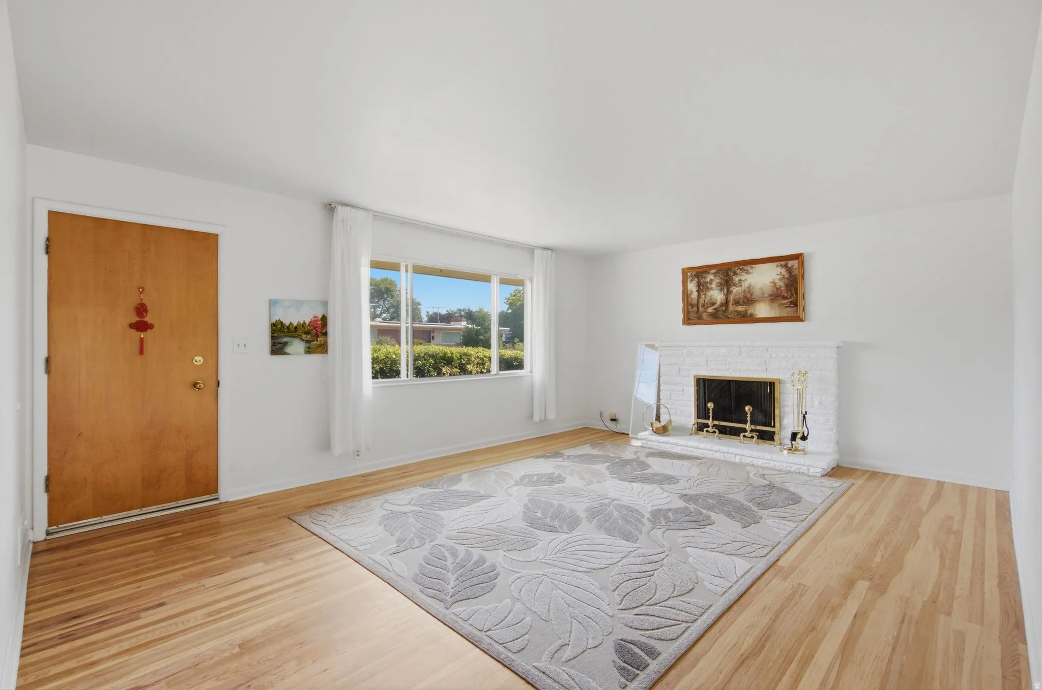 Light wood-finish flooring complements the white brick fireplace with a brass firebox