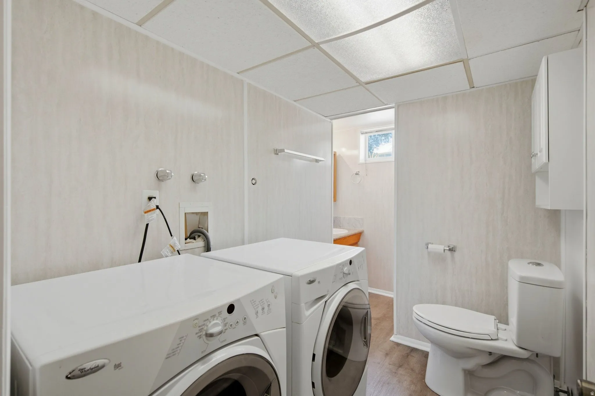 Dedicated laundry area featuring a white front-load washer and dryer, adjacent to a full bathroom with wood-finish flooring
